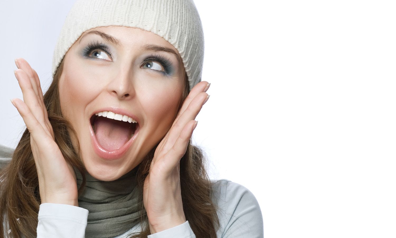 A young, brunette woman holding her hands to her face with a wide-open smile looks up in surprise.